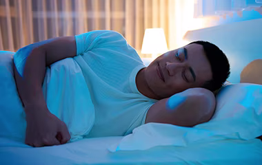 A man sleeping peacefully in a bed with blue lighting