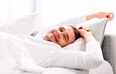 Young man smiling and stretching in bed after waking up
