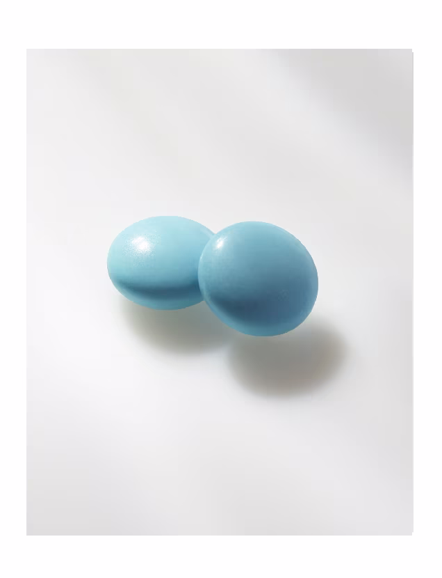 Close-up of two round blue tablets placed on a smooth white surface.